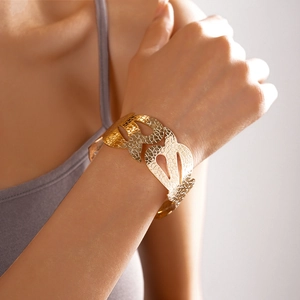 Dettaglio ravvicinato di un ampio bracciale rigido dorato con intricati motivi a fiori cavi