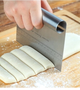 Close-up of stainless steel dough cutter with measurement markings on a wooden board