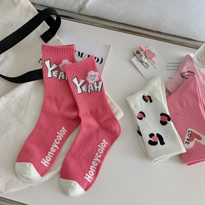 Detail view of pink cotton crew socks featuring cute heart and letter prints on white desk
