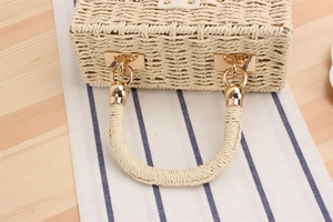 Close-up of golden metal buckle and woven texture on a natural straw box bag