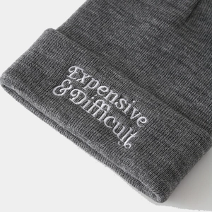 Dark grey ribbed beanie with white gothic embroidery reading Expensive & Difficult