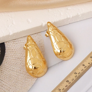 Macro detail of gold teardrop earrings with textured relief surface and metallic glow