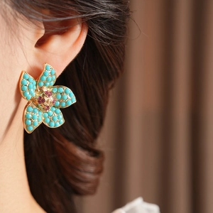 Close-up of vintage floral earrings with turquoise petals and pink gemstones on ear