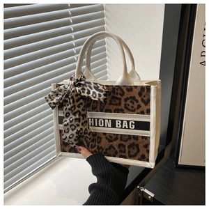 Detailed close-up of brown leopard print tote bag with cream handles and bow charm