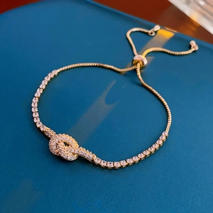 Detailed close-up of gold plated knotted bracelet with sparkling cubic zirconia on blue surface