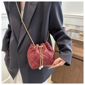 Detail of red quilted bucket bag featuring gold chain strap and pearl drawstring toggle