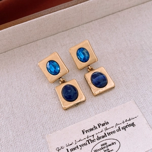 Close-up of vintage matte gold earrings with blue stones on a soft fabric texture