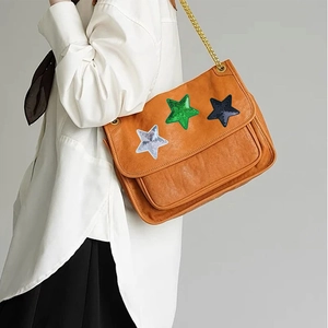 Detail of sequin star patches and gold chain strap on a brown leather shoulder bag