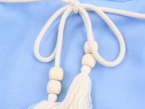 Detail of bohemian braided rope waist belt with wooden beads and tassels on blue fabric