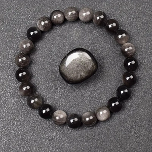 Macro view of 8mm natural obsidian beads and polished stone on a textured surface