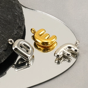 Minimalist stainless steel bubble initial pendants in gold and silver on reflective surface