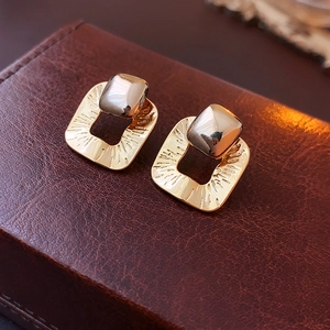 Close-up of textured gold square earrings on a premium brown leather jewelry box