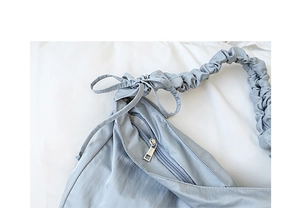 Close-up of light blue nylon bag with pleated shoulder strap and bow ribbon detail
