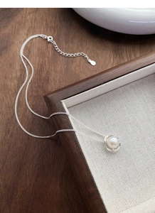 Detail of silver necklace featuring round freshwater pearl in textured wave-shaped pendant