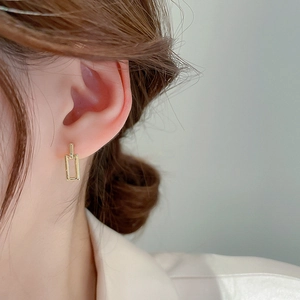 Close-up of a model wearing gold geometric interlocking rectangular stud earrings