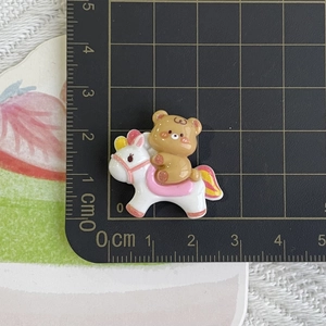 Detail view of a resin brown bear on a white horse measured at 3cm with a black ruler