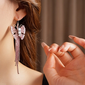 Dettaglio dell'orecchino a farfalla in zircone rosa con lunghe nappe su sfondo morbido