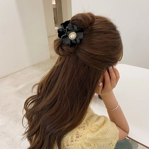 Elegant black flower claw clip with a centered pearl on long wavy hair in a cozy setting