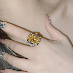 Macro shot of an ornate silver ring with a large yellow square gem worn on a hand