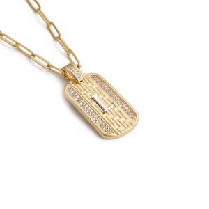 Détail du pendentif croix dorée avec lettre I argentée et cristaux sur fond blanc