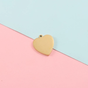 Close-up of a polished gold heart pendant on a pink and blue background for DIY jewelry