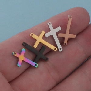 Five assorted stainless steel cross jewelry connectors held in palm for DIY crafts