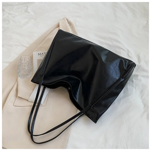 Detail of black glossy faux leather tote bag with a wrinkled texture on a white cloth