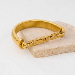 Detail of a gold snake chain bracelet on a stone with H-link and ribbed elastic band