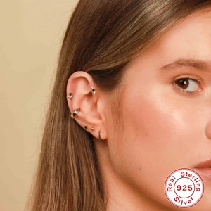 Macro detail of model wearing stacked 925 sterling silver heart and chain cartilage earrings