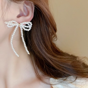 Detail of elegant pearl bow earrings with dangling tassels on a model's ear