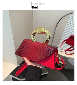 Detail of red crocodile pattern handbag with a thick golden circular metal handle