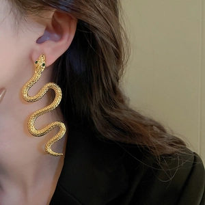 Close-up of golden snake drop earrings with green gemstone eyes on model's ear