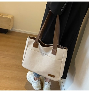 Detail of canvas tote bag showing wide brown handles and reinforced leather patches