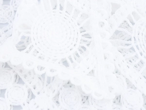 Macro shot of white hollow lace fabric with intricate floral crochet patterns on shirt