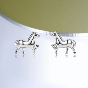 Minimalist sterling silver horse stud earrings on a reflective surface with green gradient background