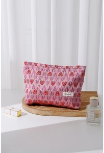 Detail of pink canvas heart patterned makeup pouch with branded label on wooden tray