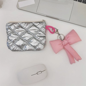 Silver quilted cosmetics pouch with pink bow keychain on a modern white desk