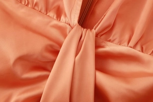 Détail de robe en satin orange avec plis torsadés et fermeture éclair invisible sur le col