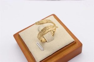 Detailed close-up of golden feather open ring showcasing fine metal textures on a beige display