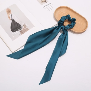 Close-up of deep teal satin hair scrunchie with ribbons on a wooden tray with a magazine