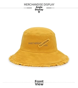 Detail view of yellow canvas bucket hat with frayed brim and embroidered patch decoration