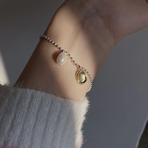 Detailed shot of a silver bead bracelet with baroque pearl and oval gold charm on a wrist