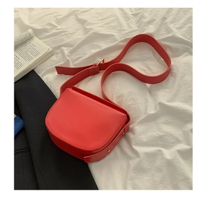 Detail of red PU leather saddle bag with wide strap on white textured background