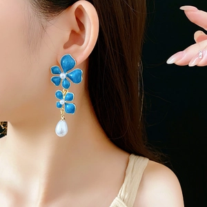 Close-up of vintage blue enamel flower earrings with pearls worn by a model