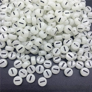 Close-up of luminous acrylic flat round alphabet beads with black minus sign for DIY crafts