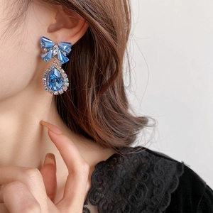 Close-up of blue crystal teardrop earrings with diamond bow design on a female model