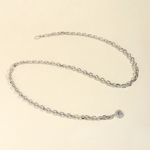 Detailed view of silver punk chain belt with lobster clasp and sun pendant on beige texture