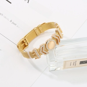 Gold mesh bracelet with rhinestone crown and gemstone charm on an aesthetic background