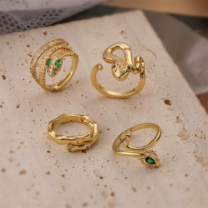 Set of four gold snake rings with green crystals and zircon on beige stone platform