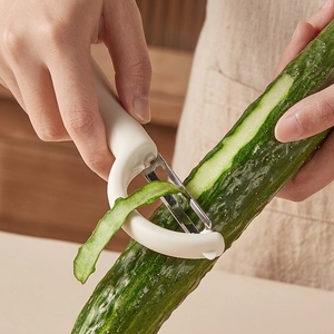 White Y-shaped stainless steel peeler slicing a fresh cucumber in a modern kitchen